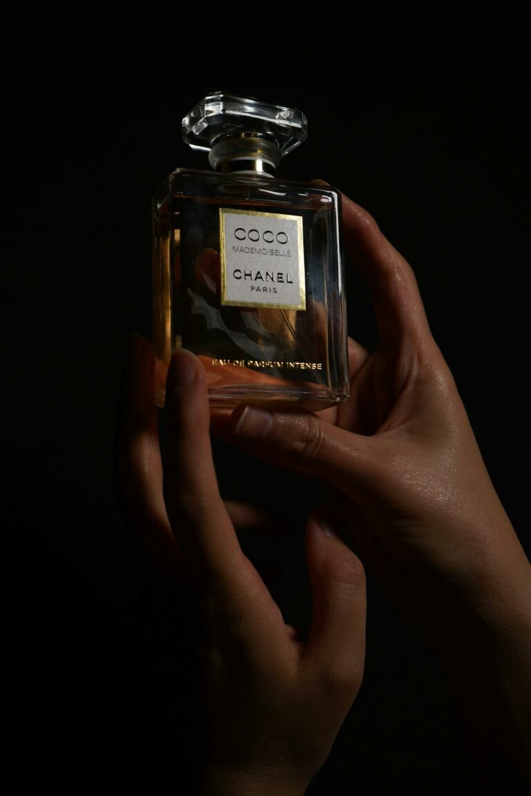 Close-up of hands holding a luxury perfume bottle against a dark background.